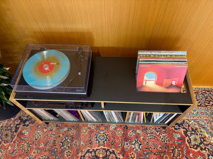 Turntable with a colorful vinyl record on a wooden shelf against a wooden wall.